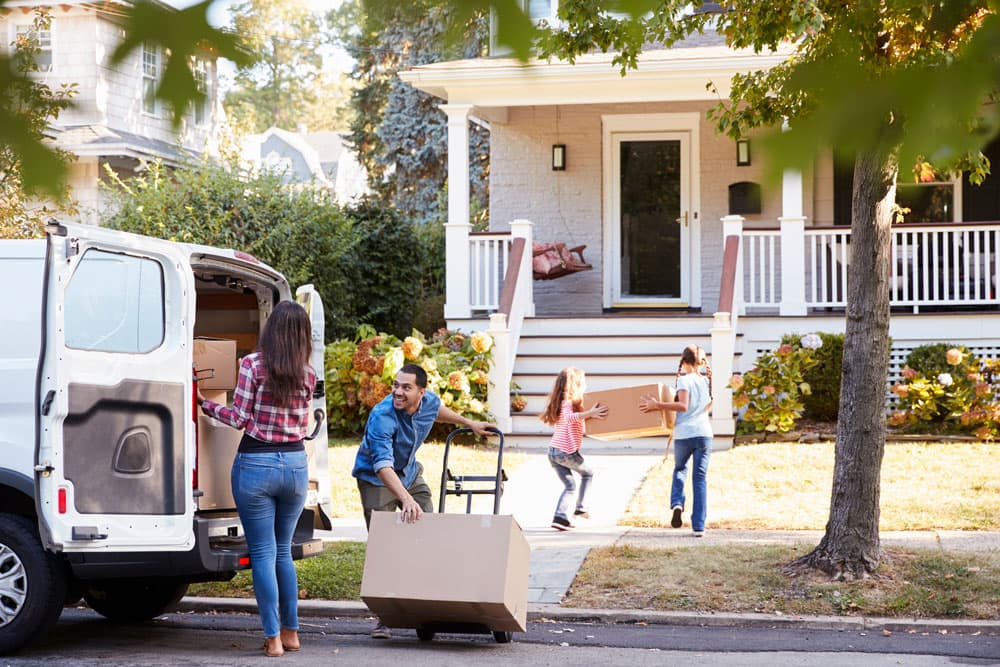 Moving boxes being unloaded from a van in front of a house