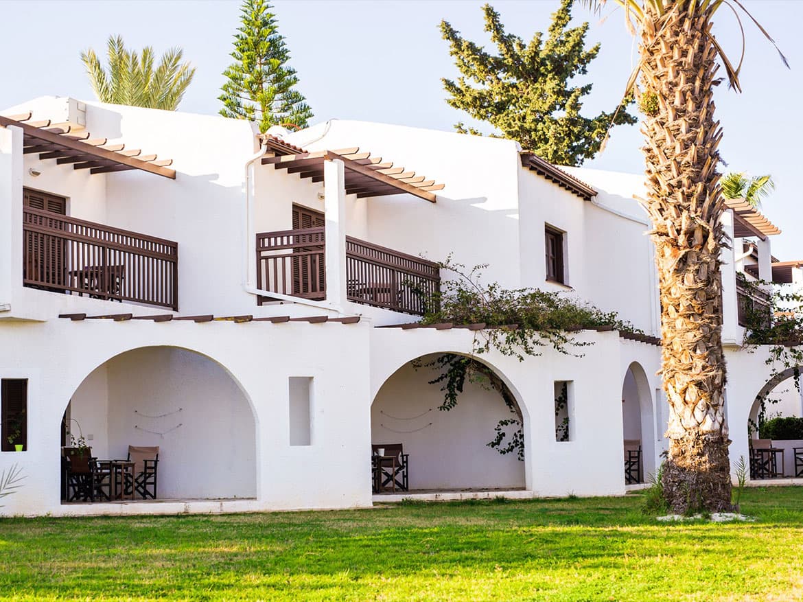 White two-story stucco building with arched porches and palm trees